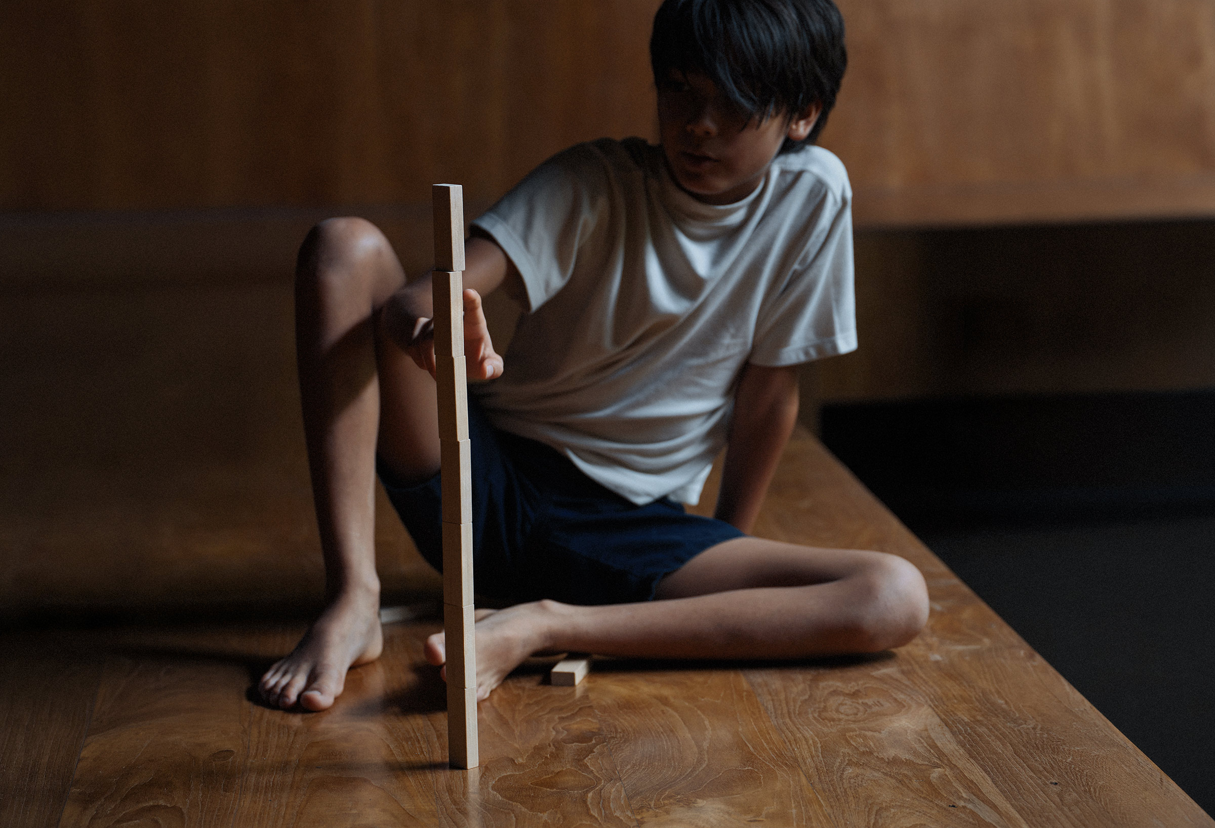 A boy leans on a sunlit table, mid-thought, in a quiet interior